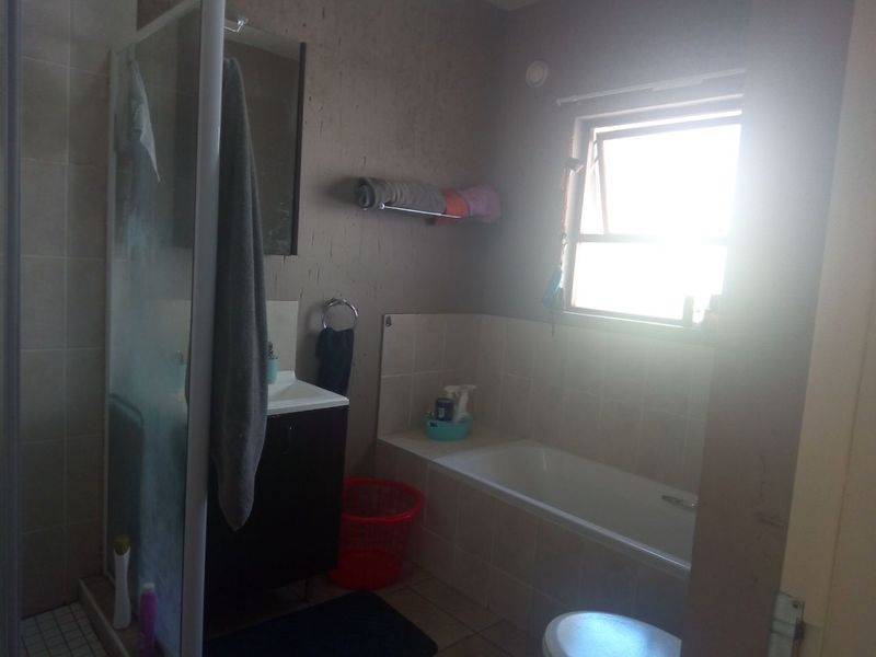 A functional bathroom featuring a shower enclosure, bathtub, and vanity cabinet, requiring cosmetic updates to improve the overall aesthetic and condition.