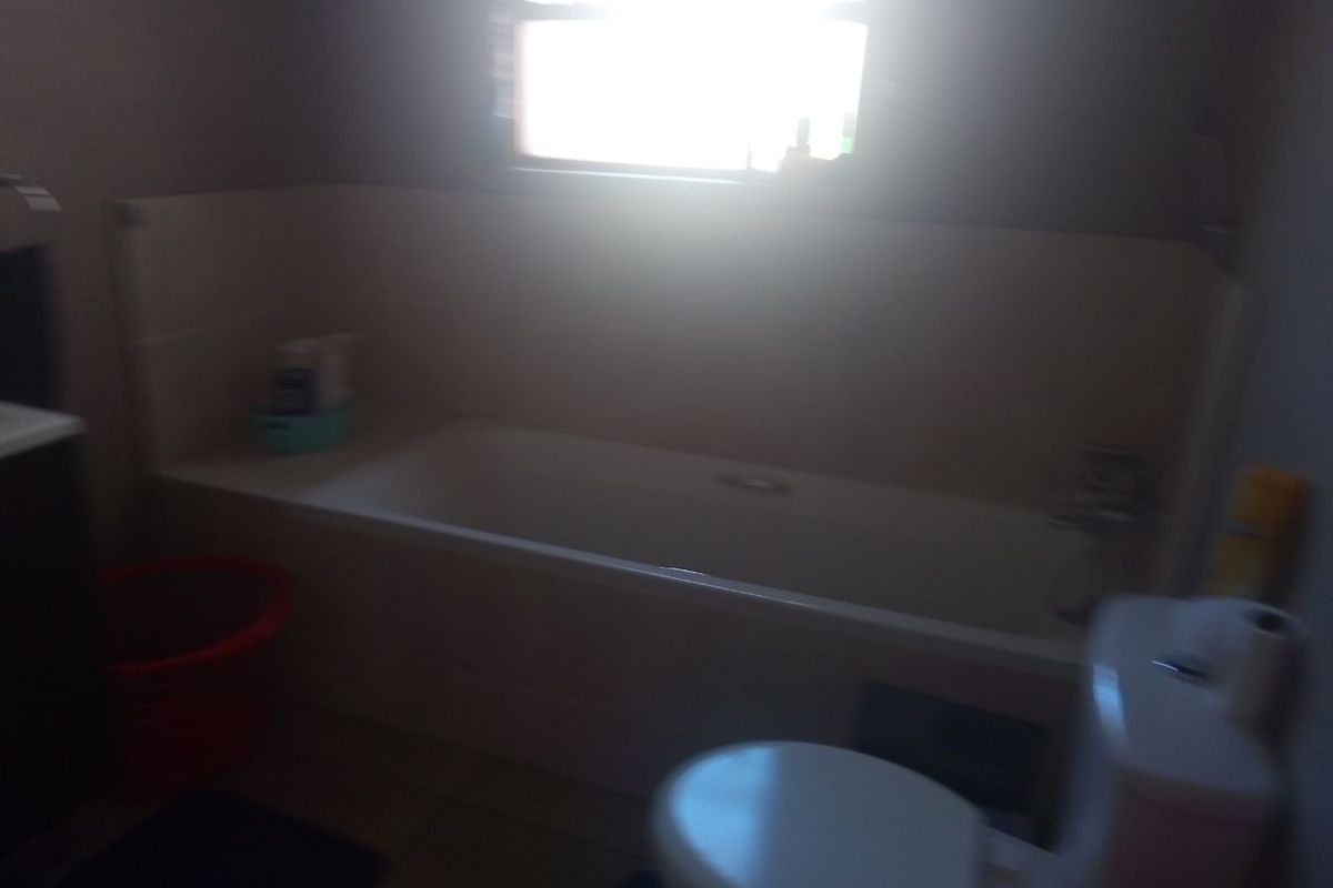 A functional bathroom featuring a standard bathtub, toilet, and tiled splashback, requiring better lighting to showcase the space effectively.