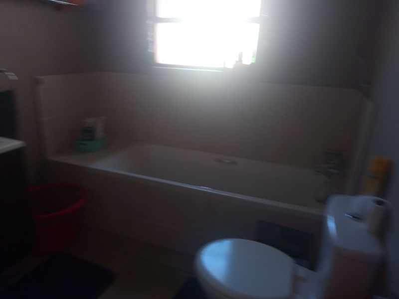 A functional bathroom featuring a standard bathtub, toilet, and tiled splashback, requiring better lighting to showcase the space effectively.