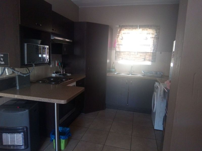 A functional kitchen featuring dark cabinetry, laminate countertops, an electric hob, and tiled flooring, providing a practical workspace for daily cooking and laundry needs.