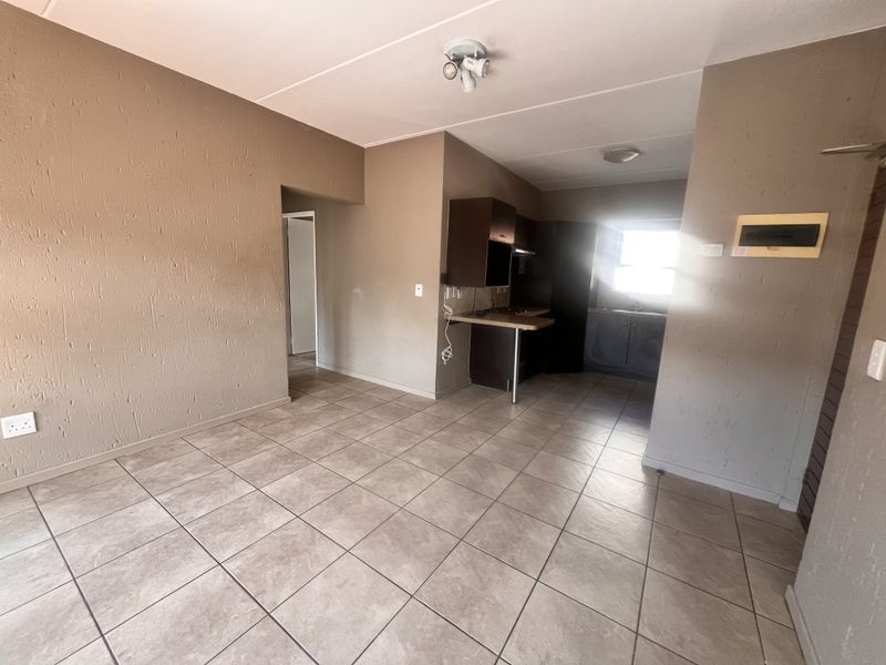An open-plan living and kitchen area featuring tiled flooring, built-in cabinetry, and a functional kitchen layout, currently vacant and ready for renovation.