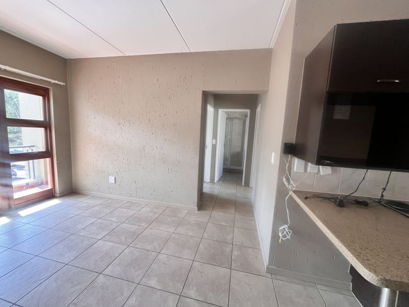 An open-plan living area featuring tiled floors, textured walls, and a partial kitchen view, leading to a hallway and balcony access.