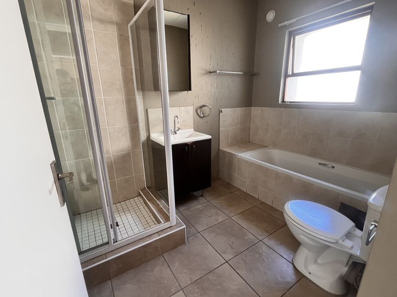 A functional bathroom featuring a separate shower enclosure, bathtub, vanity cabinet with basin, and tiled finishes throughout.