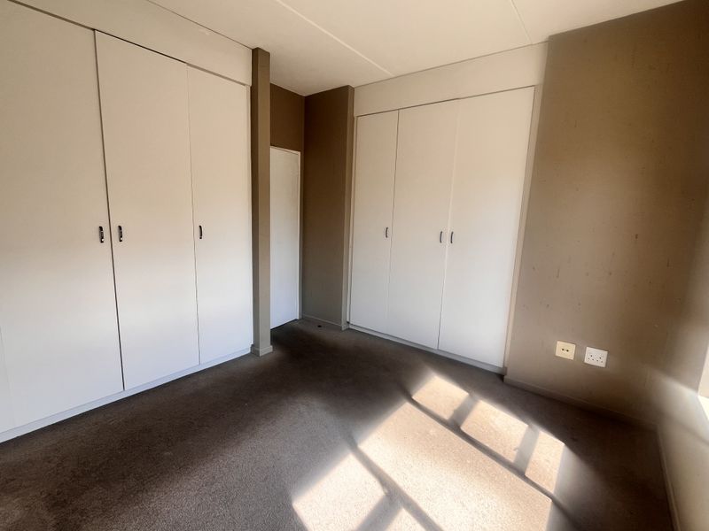 An empty bedroom featuring neutral walls, carpeted flooring, and ample built-in cupboard storage space.