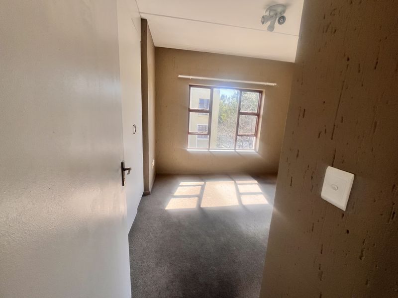 An empty bedroom featuring carpeted flooring, a built-in cupboard, and a window allowing natural light.