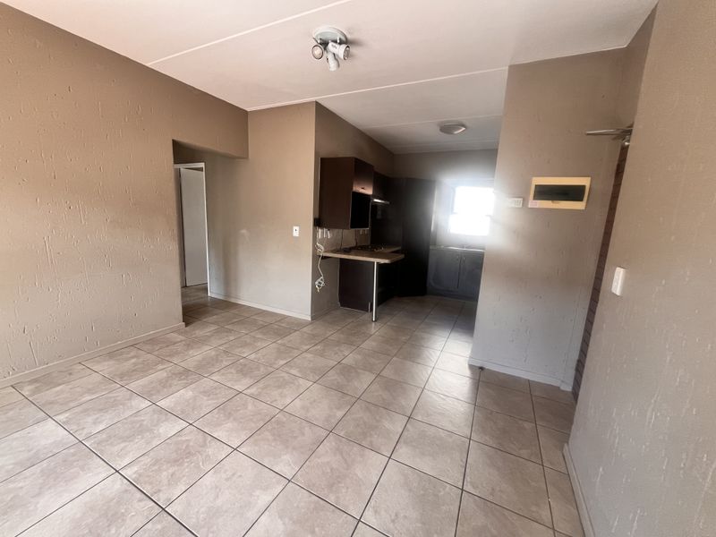 An open-plan living and kitchen area featuring tiled flooring, built-in cabinetry, and neutral wall finishes in a vacant apartment setting.