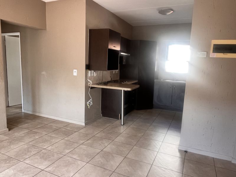 A compact, empty kitchen featuring dark built-in cabinetry, laminate countertops, and tiled flooring, requiring cosmetic updates to improve its overall appeal.