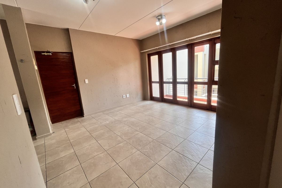 An empty, open-plan living area featuring neutral tiled flooring, a wooden door, and large glass sliding doors providing access to an outdoor space.
