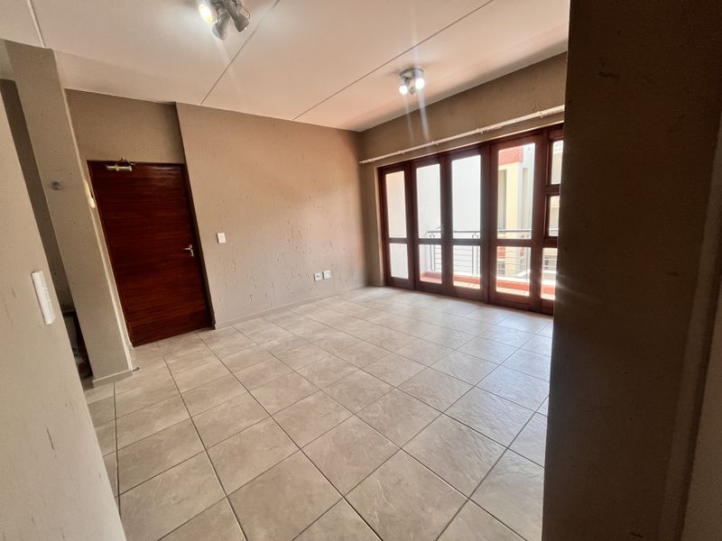 An empty, open-plan living area featuring neutral tiled flooring, a wooden door, and large glass sliding doors providing access to an outdoor space.