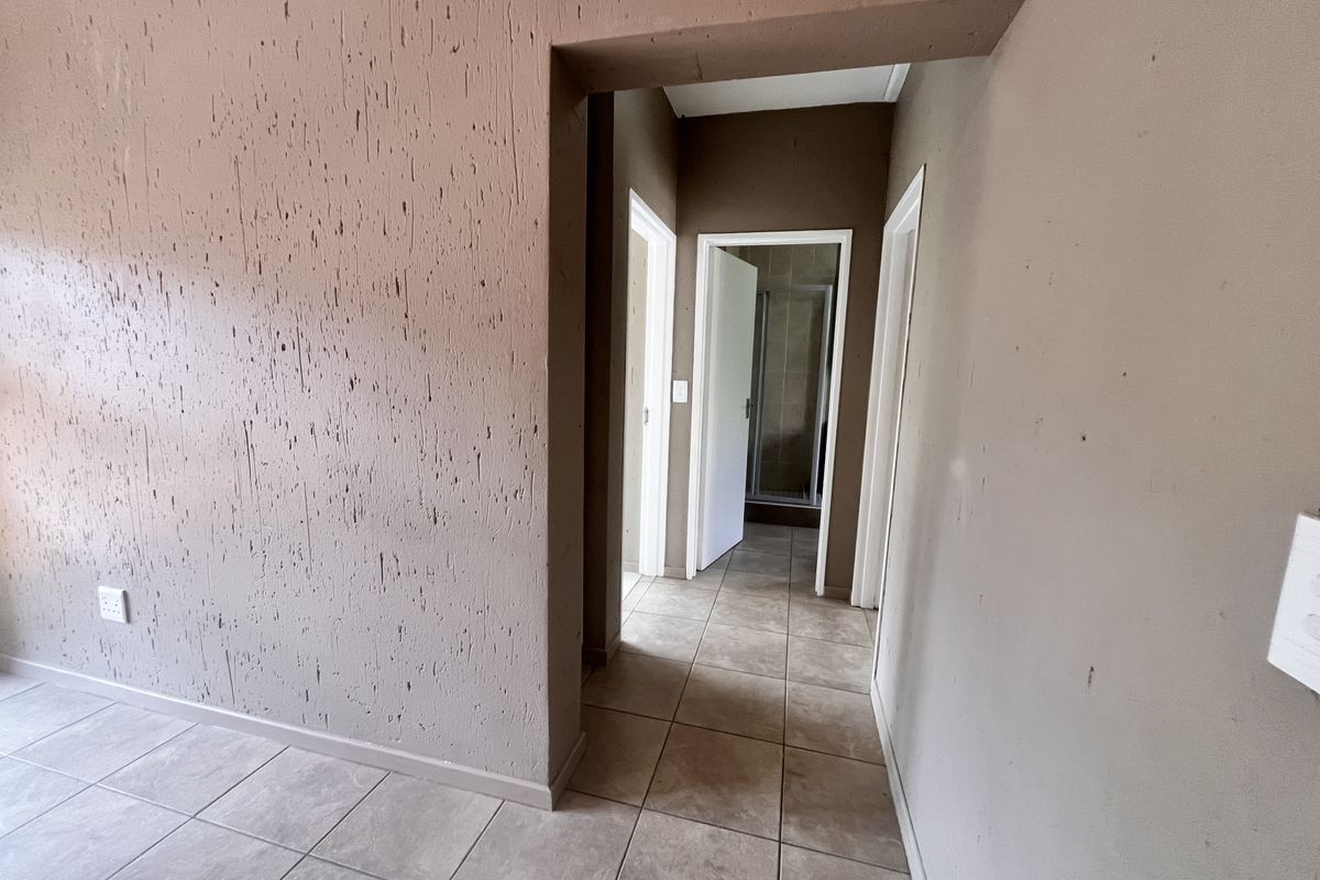 A vacant hallway featuring tiled flooring and textured wall finishes, providing access to adjacent rooms including a bathroom.