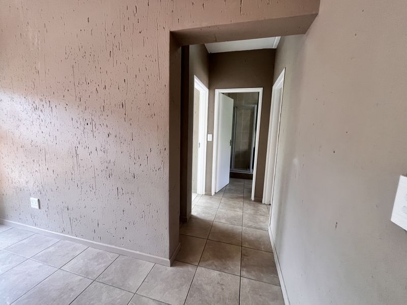 A vacant hallway featuring tiled flooring and textured wall finishes, providing access to adjacent rooms including a bathroom.