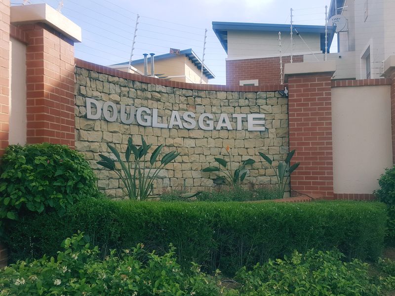 The entrance facade of the Douglasgate complex featuring a stone-clad signage wall, brick pillars, and established garden landscaping.