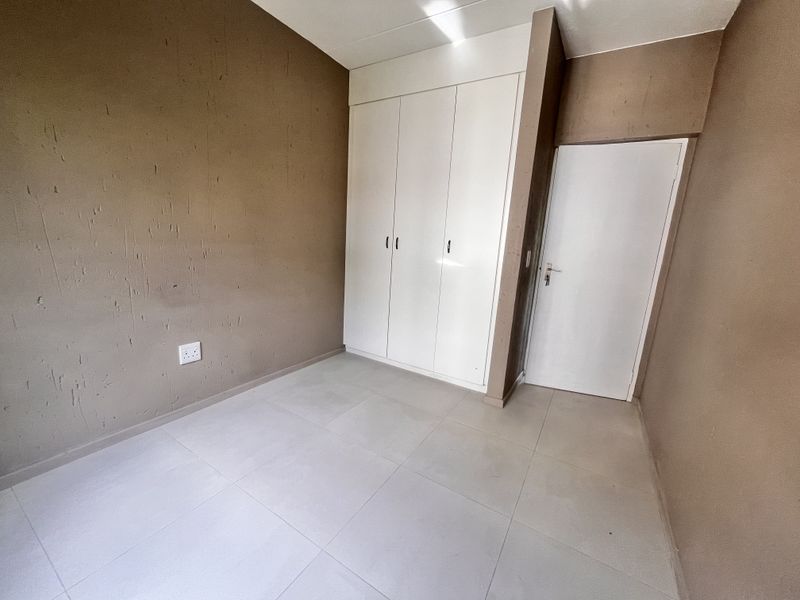 An empty bedroom featuring tiled flooring and a built-in white wardrobe with a neutral wall finish.