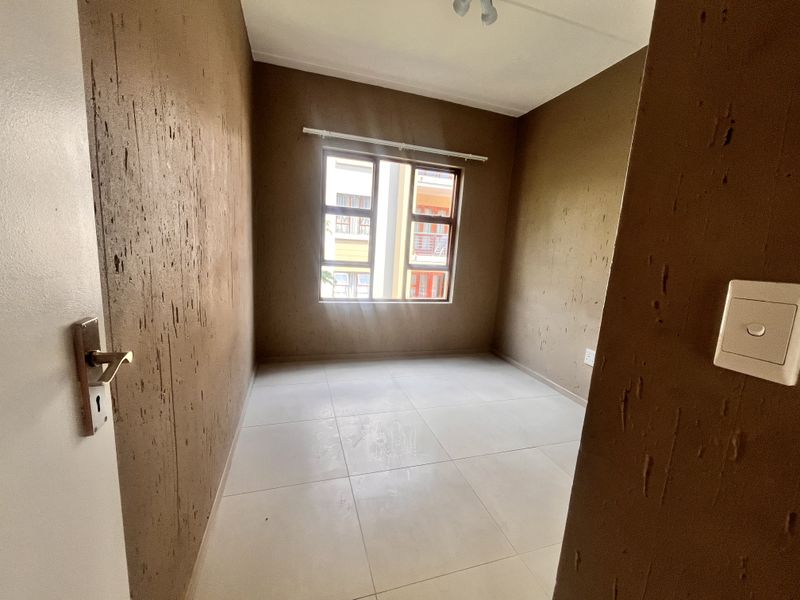 An empty bedroom featuring tiled flooring and textured brown walls with a window providing natural light.