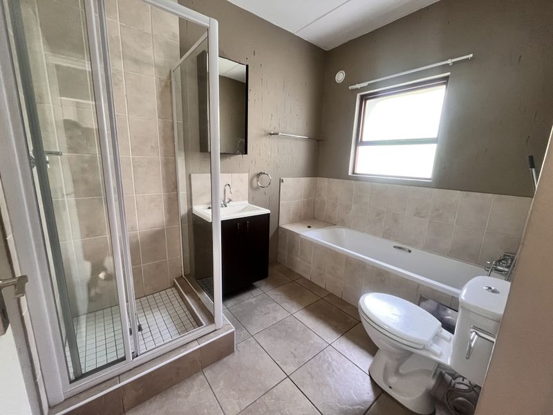 A functional bathroom featuring a separate shower enclosure, bathtub, vanity basin, and toilet with neutral floor tiling and painted walls.