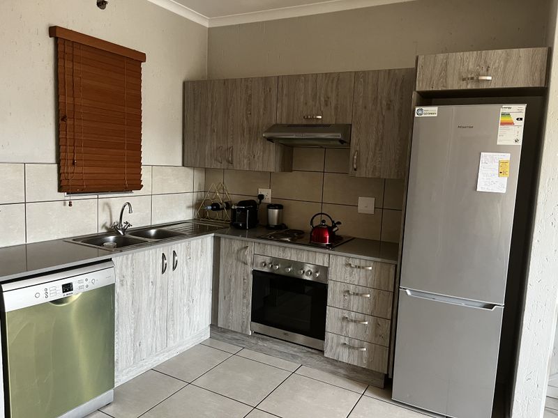 A functional kitchen featuring wood-look cabinetry, stainless steel appliances including an oven and hob, tiled backsplash, and neutral floor tiles.