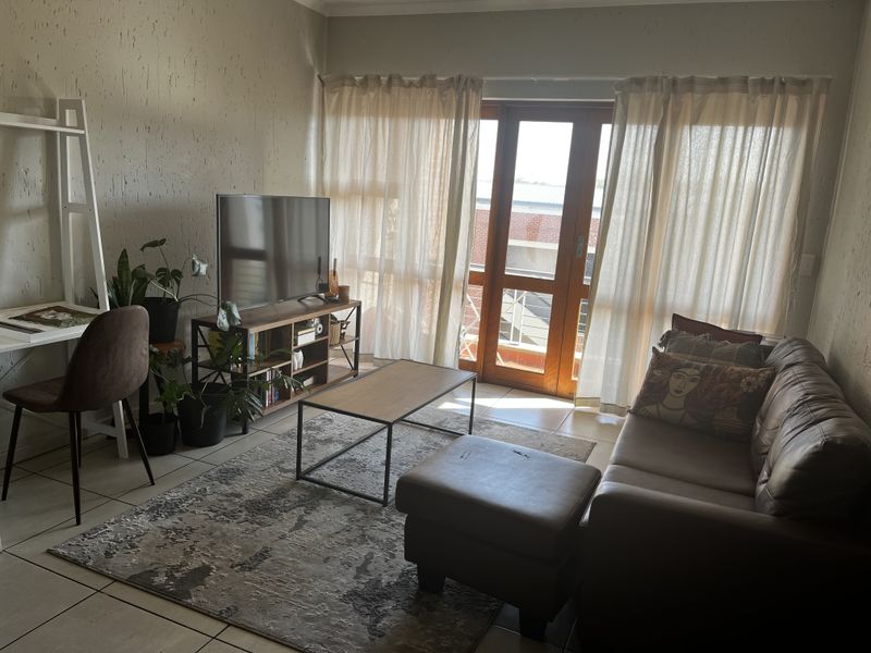 A comfortable living room featuring tiled flooring, textured walls, and a timber-framed glass door providing access to an outdoor area.