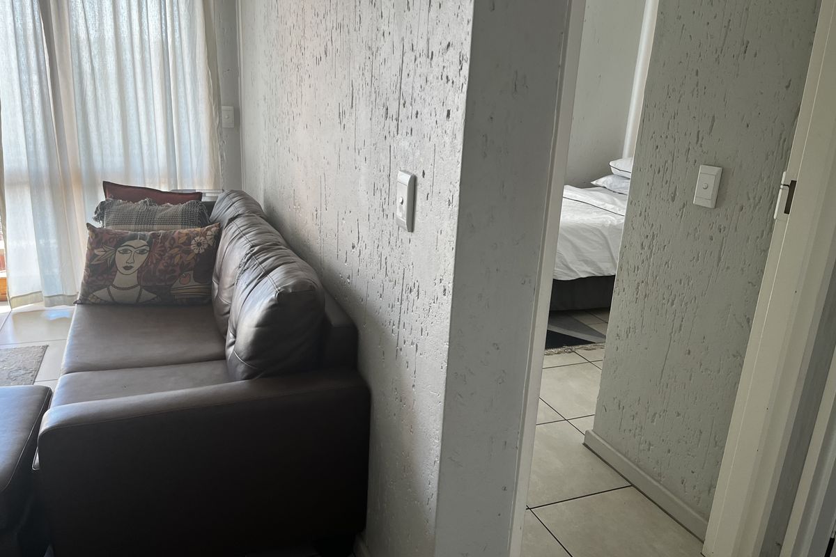 Living area featuring textured wall finishes and ceramic floor tiles, with a view into the adjacent bedroom space.