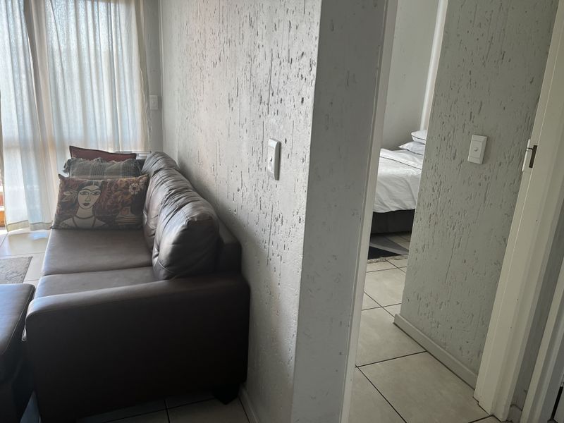 Living area featuring textured wall finishes and ceramic floor tiles, with a view into the adjacent bedroom space.