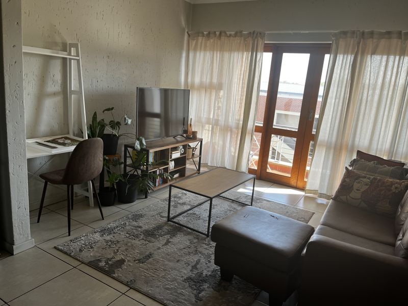 A living room featuring tiled flooring, textured walls, and a wooden framed glass door leading to an outdoor area.