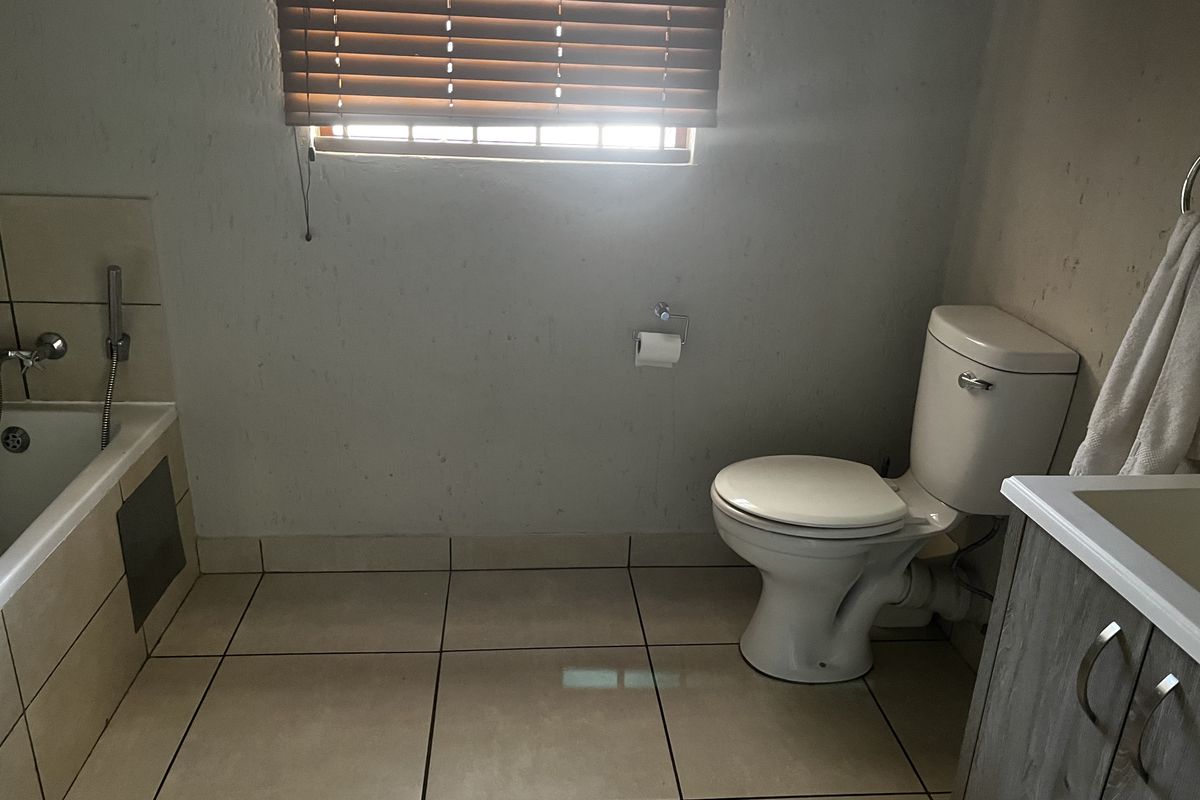 A functional bathroom featuring a built-in bathtub, toilet, and vanity cabinet with tiled flooring and window blinds.