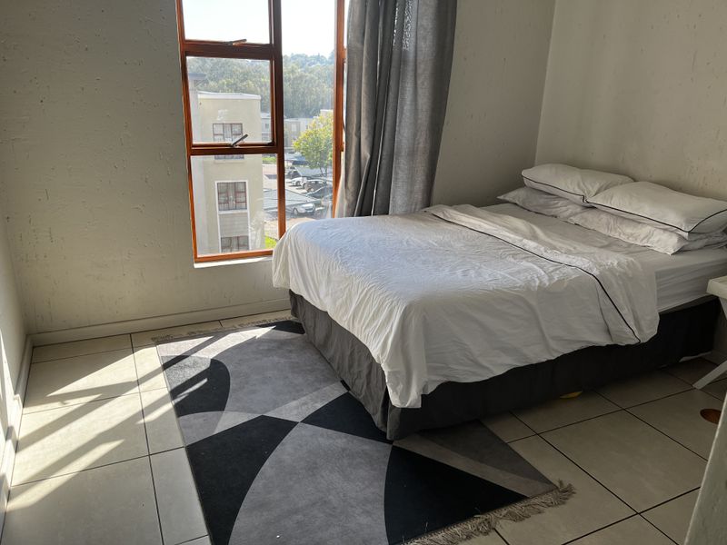 A bedroom featuring tiled flooring and a large window with natural light, showing some signs of wear on the wall surfaces.