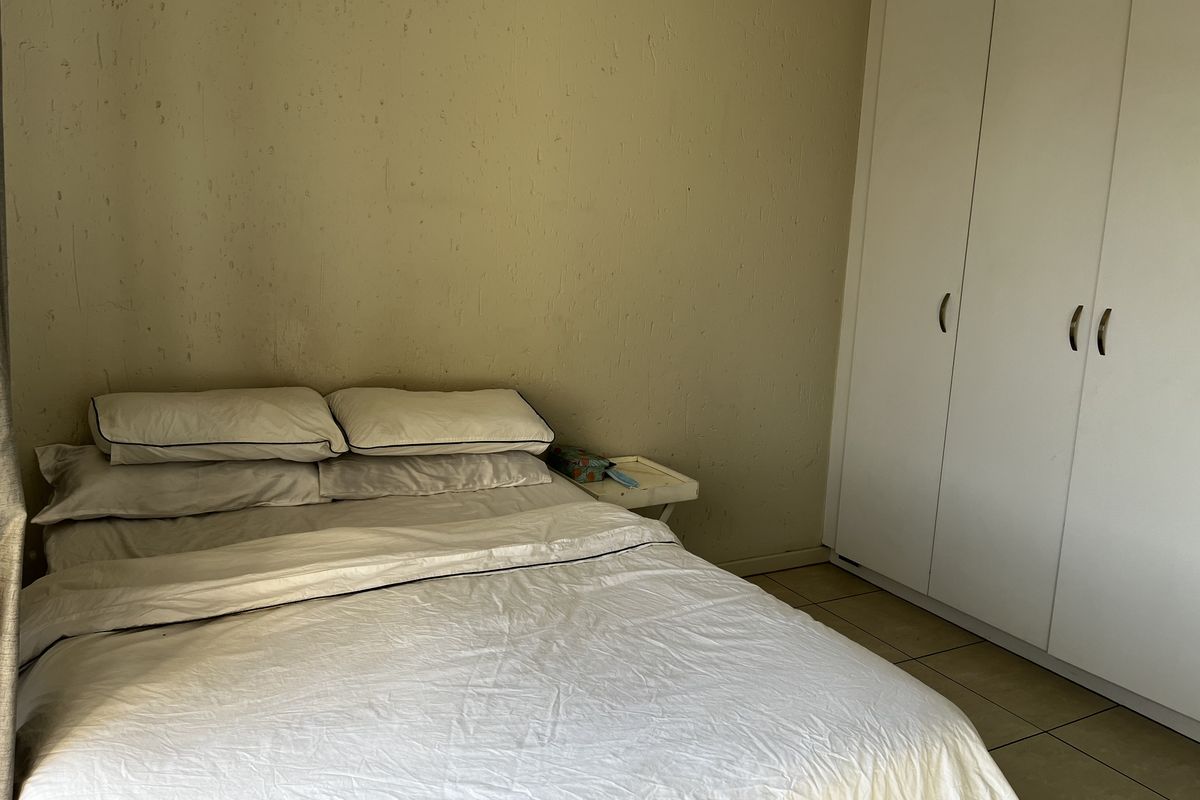 A bedroom featuring tiled flooring and a built-in wardrobe, showing signs of wear on the wall surfaces.