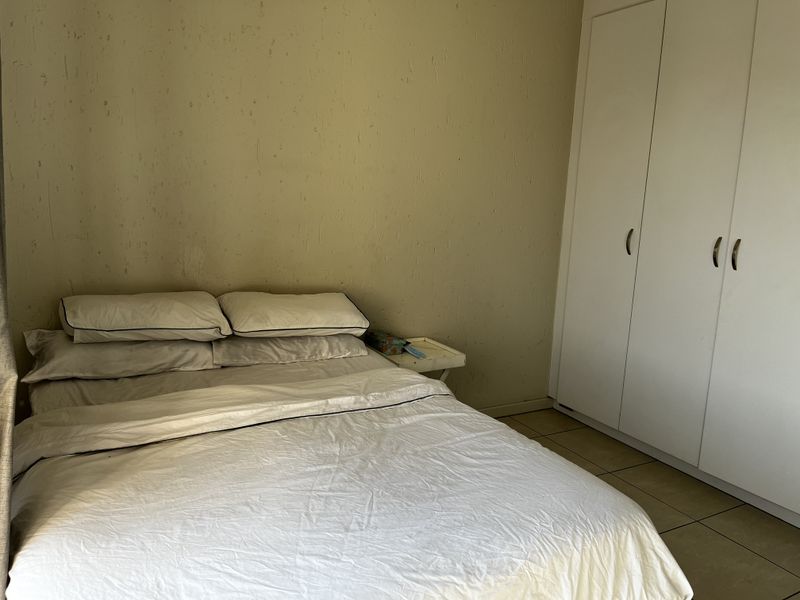 A bedroom featuring tiled flooring and a built-in wardrobe, showing signs of wear on the wall surfaces.