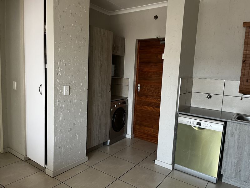 A functional kitchen area featuring built-in cabinetry, tiled flooring, a tiled backsplash, and integrated dishwasher and washing machine appliances.