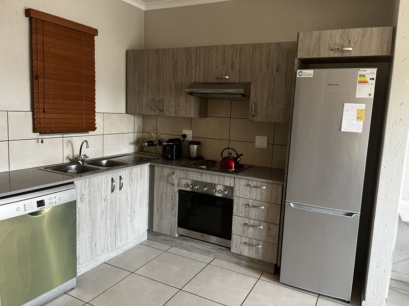 A functional kitchen featuring wood-look laminate cabinetry, stainless steel appliances including an oven and hob, tiled splashbacks, and neutral floor tiles.