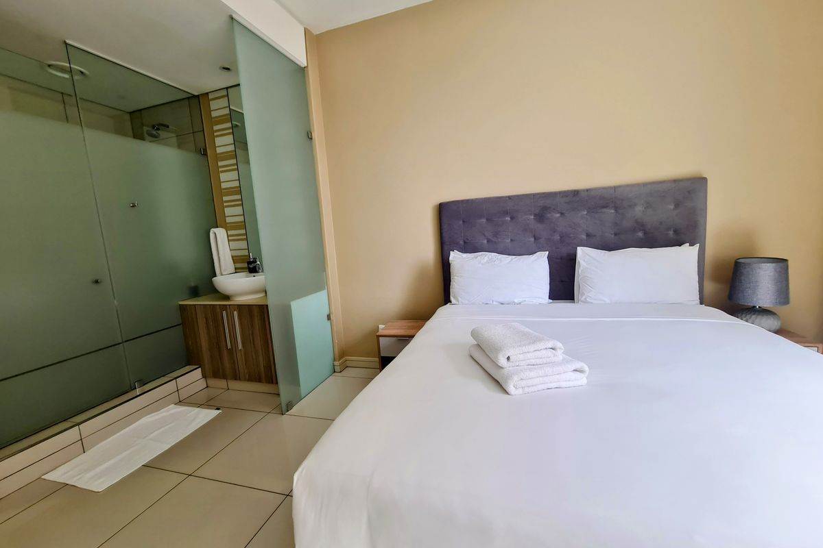 A bedroom featuring an open-plan en-suite bathroom with a glass shower enclosure and a modern vanity unit.