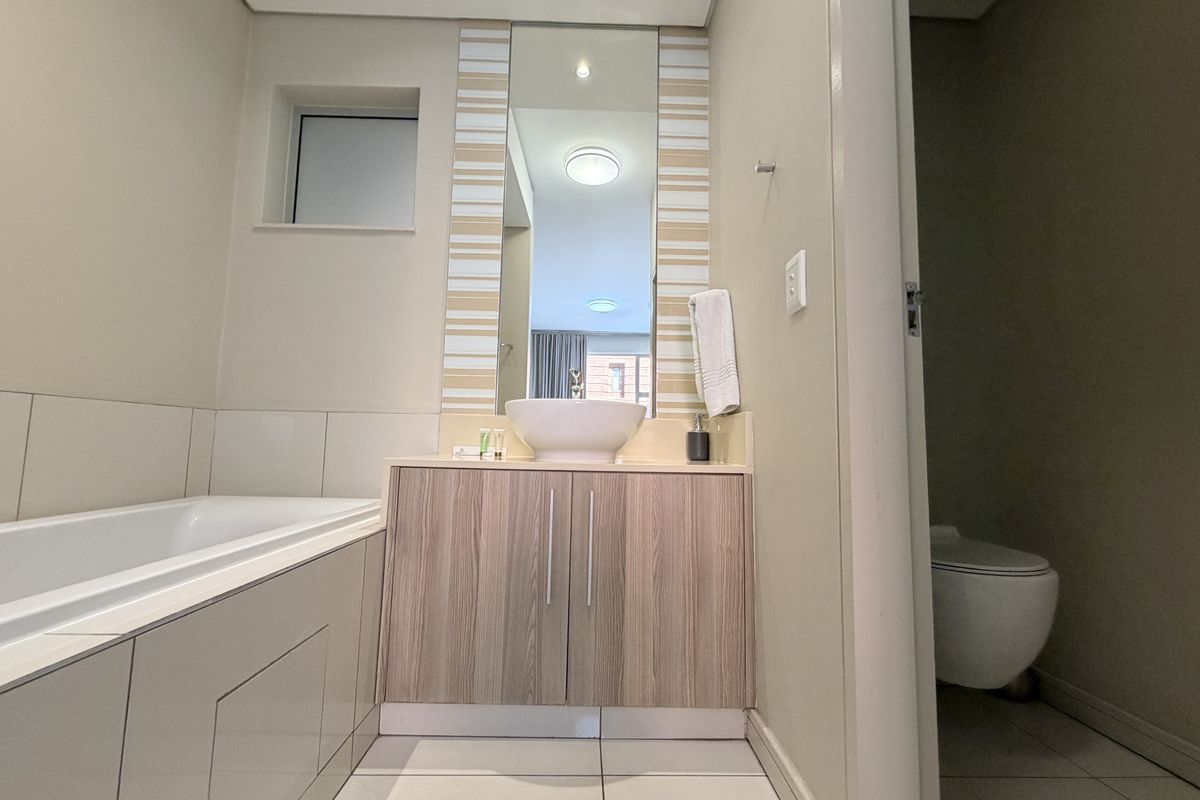 Modern bathroom featuring a built-in vanity with vessel sink, a tiled bathtub, and a separate enclosed toilet area with neutral finishes.