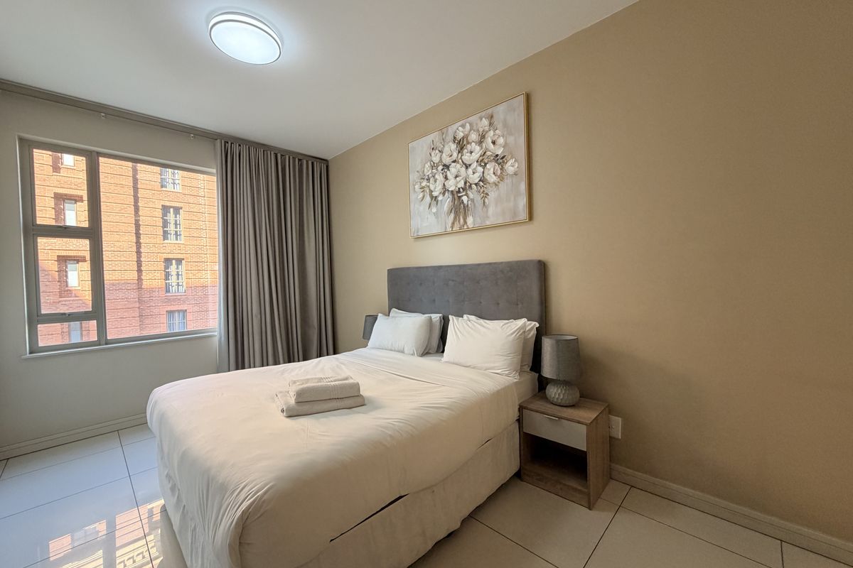 A well-maintained bedroom featuring tiled flooring, a large window providing natural light, and neutral wall tones.