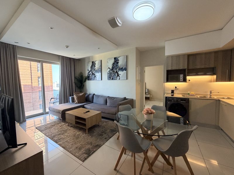 Modern open-plan living area featuring a compact kitchen with built-in cabinetry, tiled floors, and direct access to a private balcony through sliding glass doors.