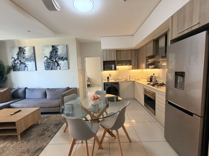 Modern open-plan living area featuring a well-appointed kitchen with built-in appliances, sleek cabinetry, and tiled flooring, seamlessly flowing into the dining and lounge space.