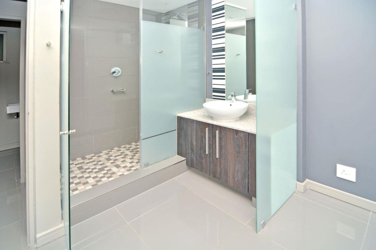 Modern bathroom featuring a walk-in shower with frosted glass enclosure, a contemporary vessel sink on a vanity cabinet, and neutral tiled finishes.