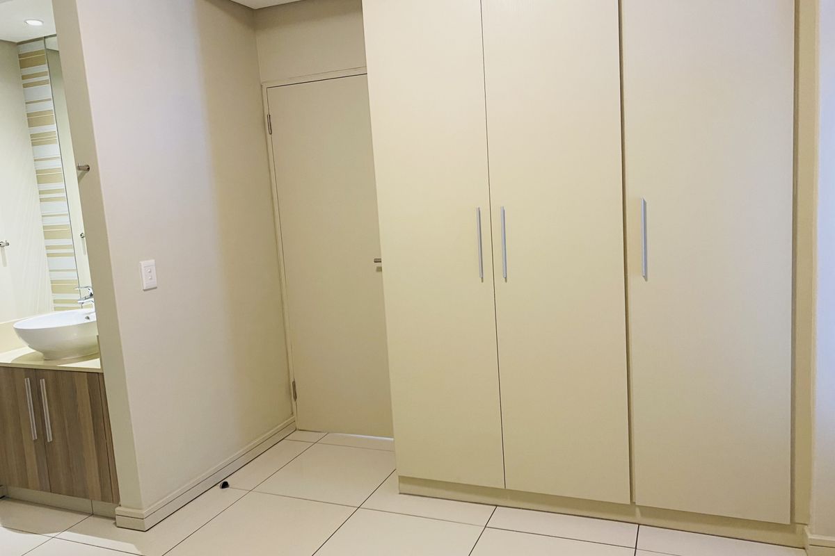 A clean bedroom interior featuring large built-in wardrobes, neutral tiled flooring, and an integrated vanity area with a modern basin.
