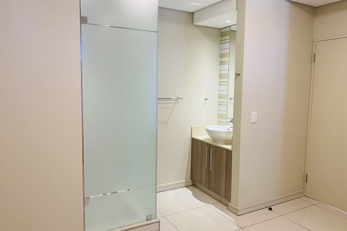 A clean, modern bathroom featuring a frosted glass shower enclosure, a vanity cabinet with a vessel sink, and neutral tiled flooring.