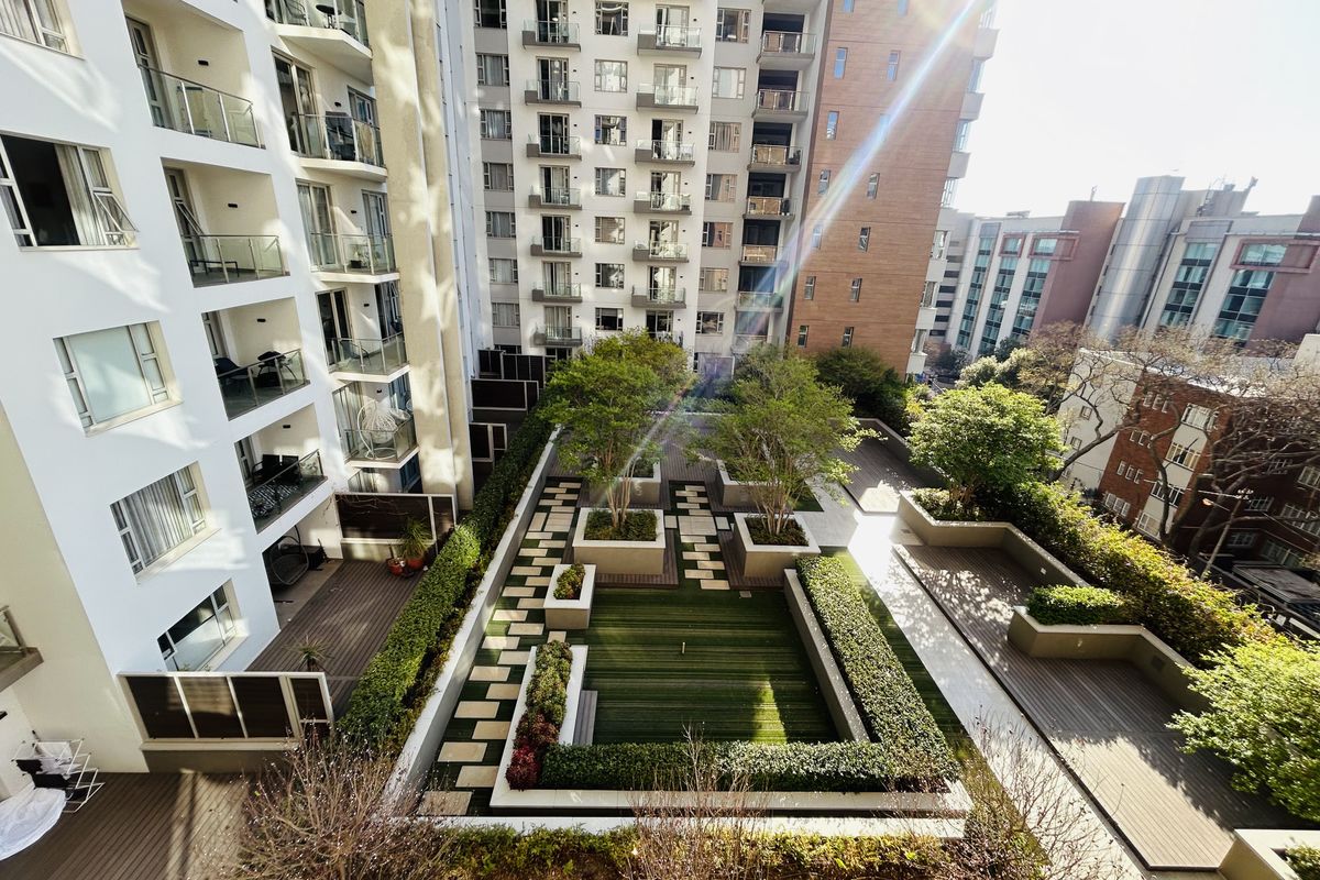 An elevated aerial view of a well-maintained apartment complex courtyard featuring landscaped gardens, timber decking, and paved pathways between residential buildings.