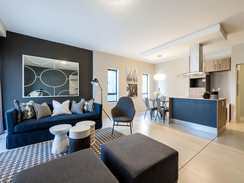 Modern open-plan living area featuring a contemporary kitchen with island, sleek cabinetry, extractor fan, and neutral tiled flooring throughout the combined space.
