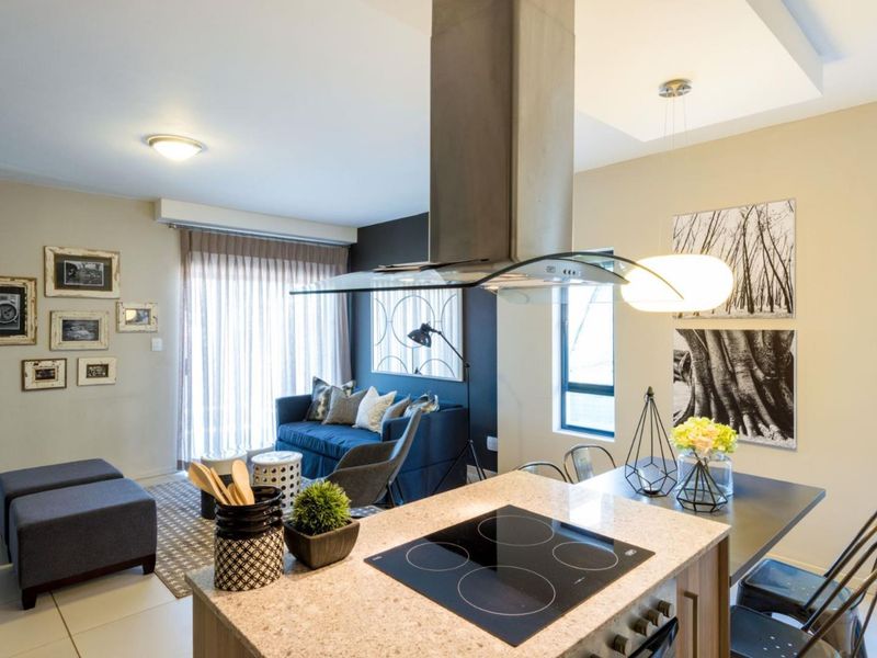 Modern open-plan living area featuring a kitchen island with an electric hob, stainless steel extractor, and stone countertops, flowing into a comfortable lounge space.