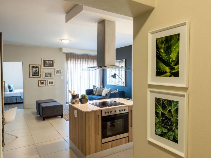 Modern open-plan living area featuring a central kitchen island with built-in appliances, tiled flooring, and seamless flow to the adjacent living space.