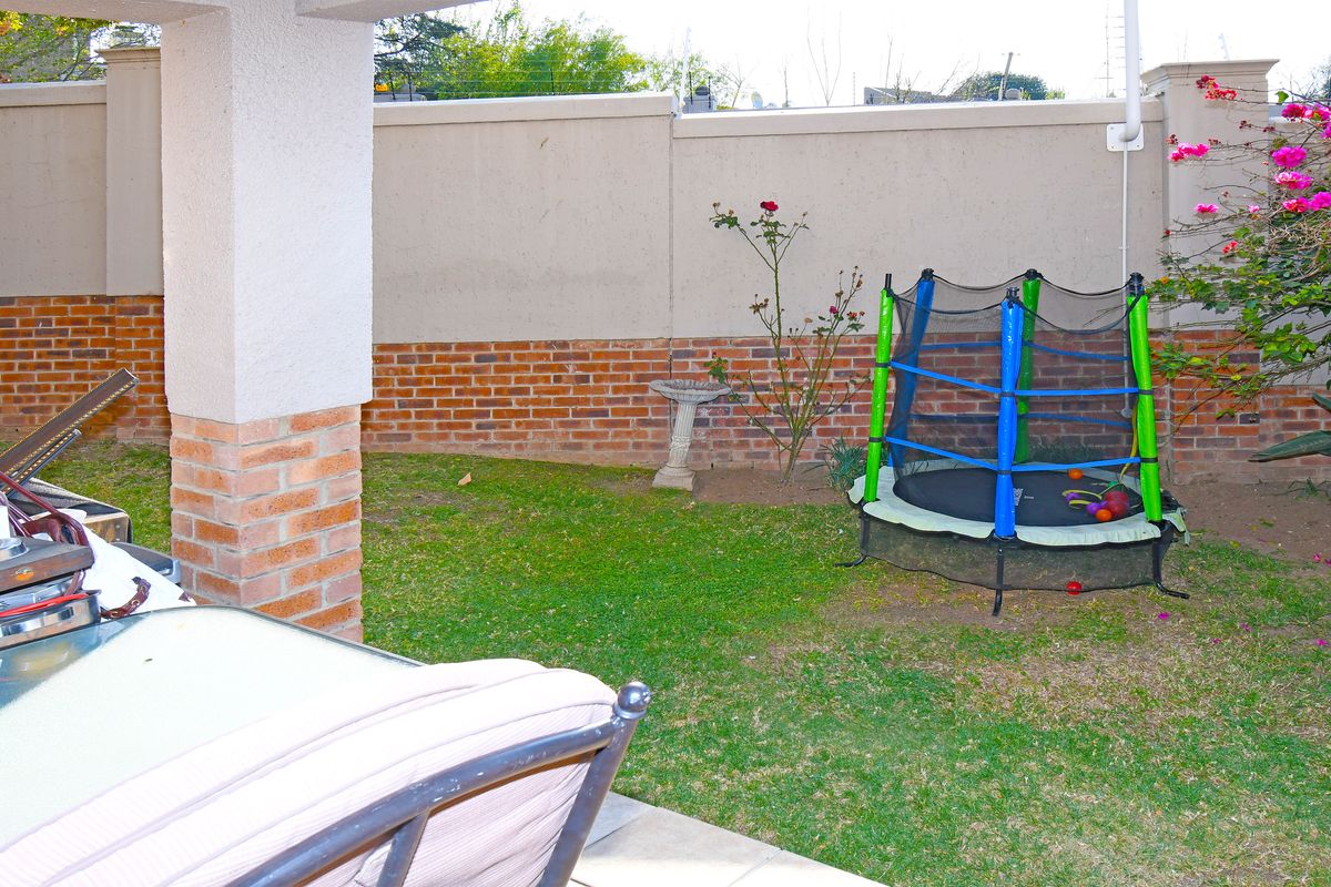 A private rear garden area featuring a covered patio section, brick boundary walls, and a small lawn space.