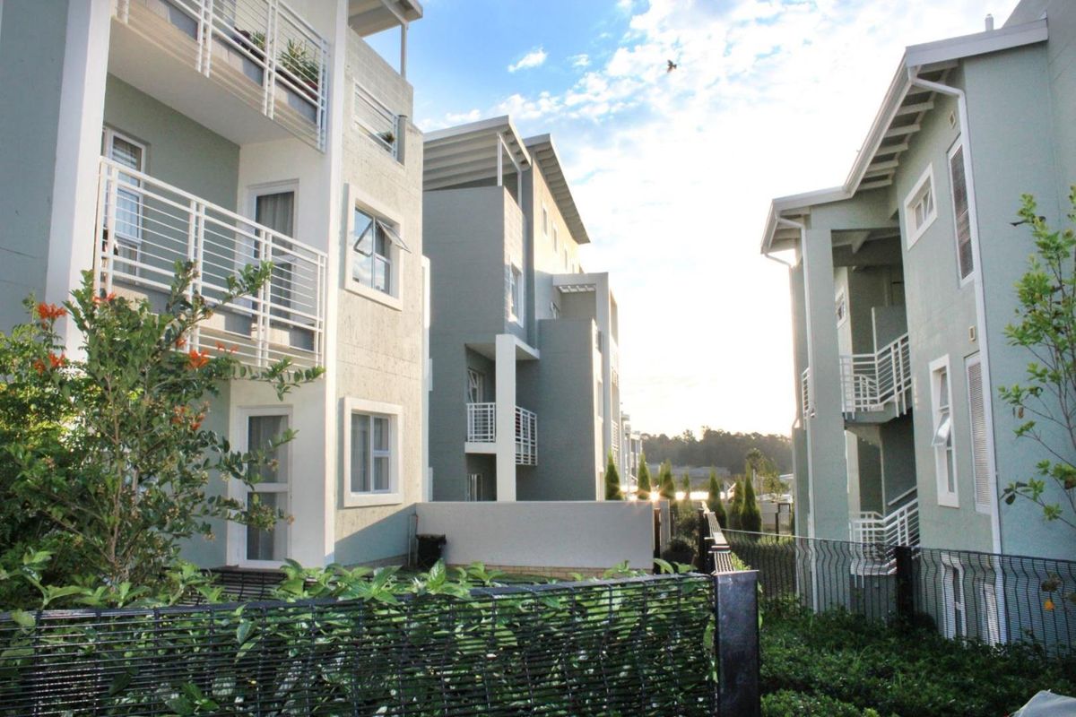 Exterior view of modern apartment blocks featuring balconies, metal railings, and landscaped garden areas within a residential complex.