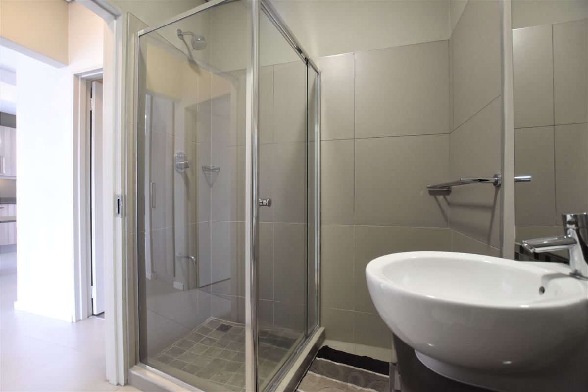 A clean, modern bathroom featuring a glass-enclosed shower, neutral wall tiling, and a contemporary basin with a chrome mixer tap.