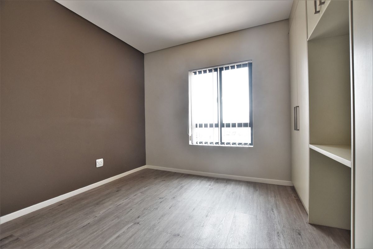 A bright, empty bedroom featuring modern laminate flooring, a neutral color palette, and a built-in wardrobe with integrated shelving.