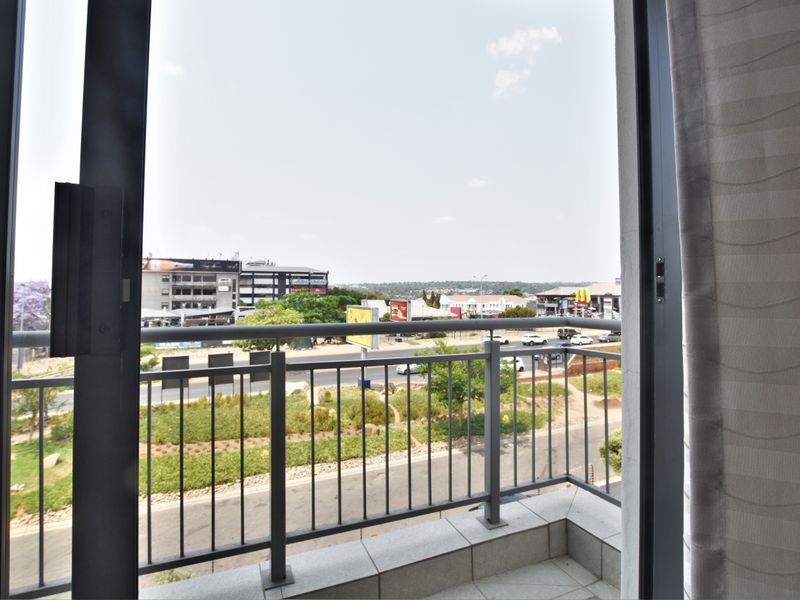 A private balcony featuring tiled flooring and a metal balustrade, offering an elevated view of the surrounding urban landscape and street.
