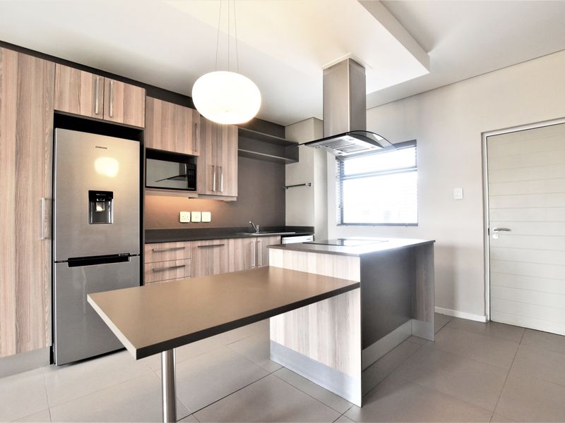 Modern kitchen featuring wood-grain cabinetry, a central island with breakfast bar, integrated appliances, and sleek tiled flooring.