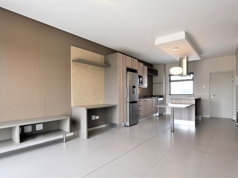 Modern open-plan kitchen and living area featuring sleek cabinetry, a central island, tiled flooring, and a built-in desk space.