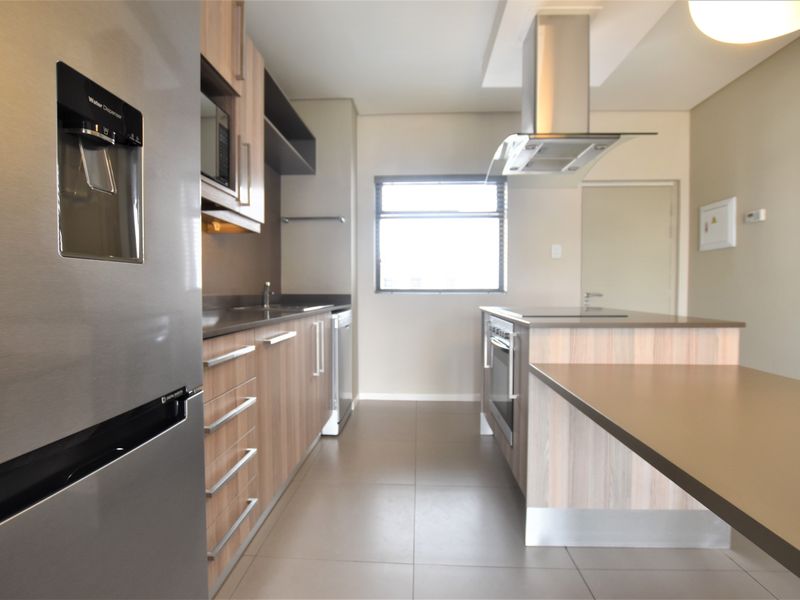 Modern kitchen featuring wood-finish cabinetry, stone countertops, stainless steel appliances, and a functional island layout with integrated hob and oven.